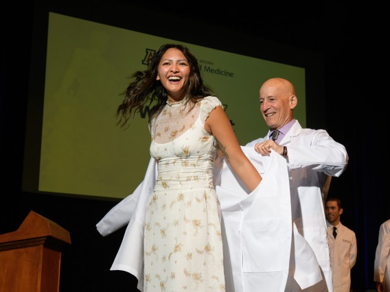 Mentor places a white coat on a student during the White Coat Ceremony