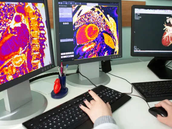 A person seated at a desk, working on a computer with two monitors displaying various applications and data.