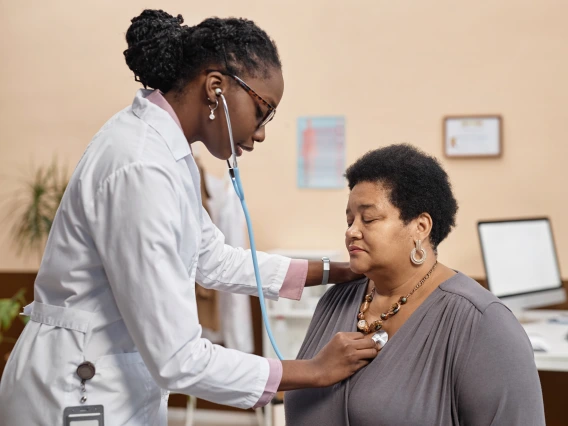 Young African American physician using stethoscope while asking senior female patient to make a deep breath during medical examination