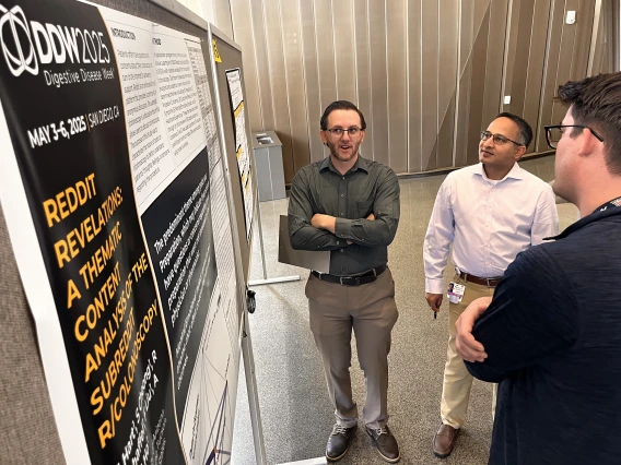 [Hospitalist Anthony Whitten, DO, asks a question about a poster, “Reddit Revelations: A Thematic Content Analysis of the Subreddit R/Colonoscopy” to Maxwell A. Hart, MD, Med, a PGY-3 IM resident, as Inpatient Medicine division chief Tejo Vemulapalli, MD, listens.]