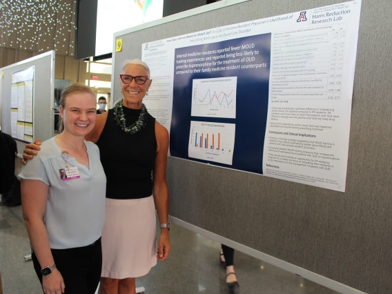 [PGY-1 IM resident Cassandra Everly, MD, MPH, with one of her co-authors Beth Myerson, MDiv, PhD, founding director of the Department of Family & Community Medicine’s Harm Reduction Research Lab, next to their poster: “How Does IM Match Up? A study of Arizona resident physicians' likelihood of prescribing medication for Opioid Use Disorder.” The center was created in 2018 to improve opioid disorder diagnoses and reduce bloodborne illnesses like HIV and hepatitis. ]
