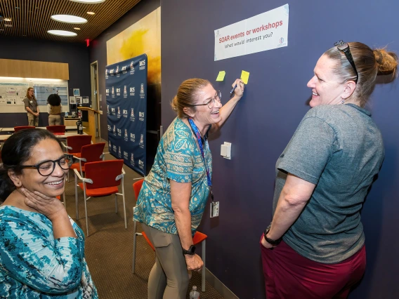 [Cardiology’s Shibani Mukerjee, PhD (left), laughs with colleagues as they come up with thoughts to add to post-its for the SOAR in DOM research forum’s “Idea Wall.”]