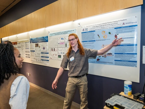 [Jesse Riemenschneider, an undergraduate student researcher with Steven Goldman, MD, talks to a SOAR in the DOM forum attendee on his poster, “Development of an electromagnetic induction wireless charging for raspberry pi pico-based atrial fibrillation device in swine.”]