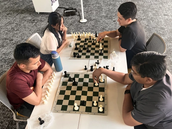 [Nathan Holt, DO (in black top – PGY-1 radiology resident), and Inpatient Medicine’s Anil Potharaju, MD (to Dr. Holt’s left), both decide to move their pawns at same time. The question is to which square.]