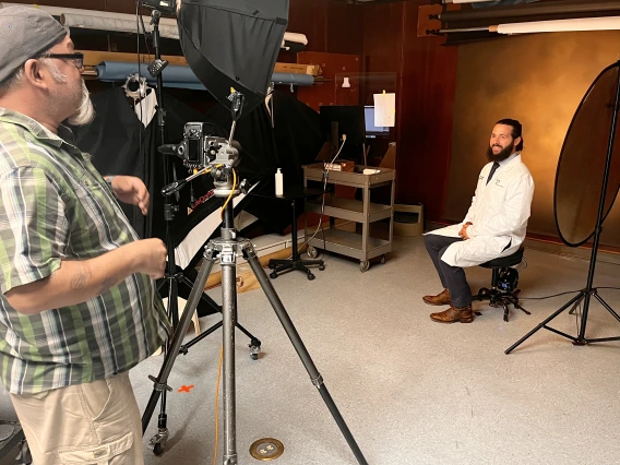 [UAHS BioCommunications photographer Mitch Masilun (left) prepares to shoot a white coat profile shot of Ethan Renfrow, DO, in the BioCom studio on the college’s third floor.]