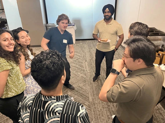 [A PGY-3 IM resident Simar Singh, MD, PhD, MS (with plate upper right), holds court at the IM Research Mixer, June 30, in the COM-T Social Hall with (to the left of him) interns Adam Weston, MD (giving thumbs up), Nellie Tolliver, MD, Joy Eskandar, MD, and others enjoying the moment.]