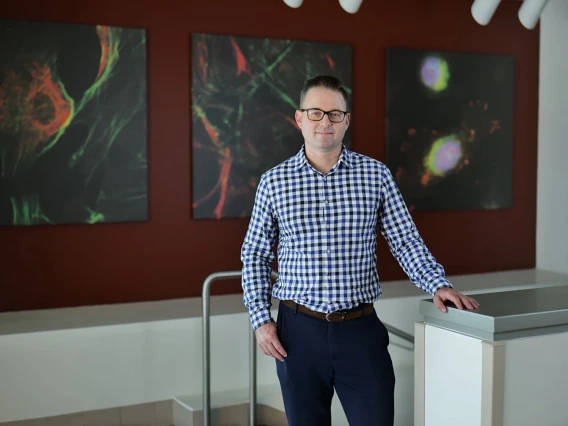 [The Division of Hematology & Oncology’s Aaron Scott, MD, standing next to a stairwell in the upper lobby of the University of Arizona Cancer Center with abstract art behind him on the wall]