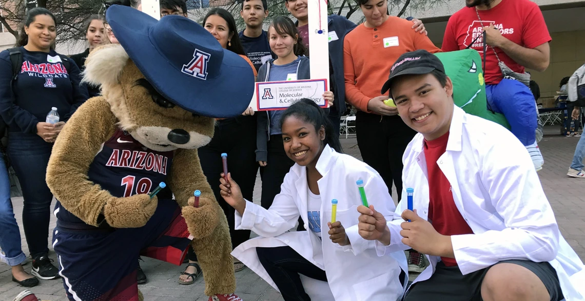 A cheerful gathering of people standing with a vibrant mascot, capturing a joyful moment at a community celebration.