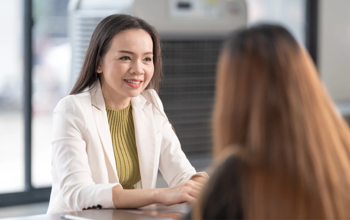 A woman in a business suit engaged in conversation with another woman in a professional setting.