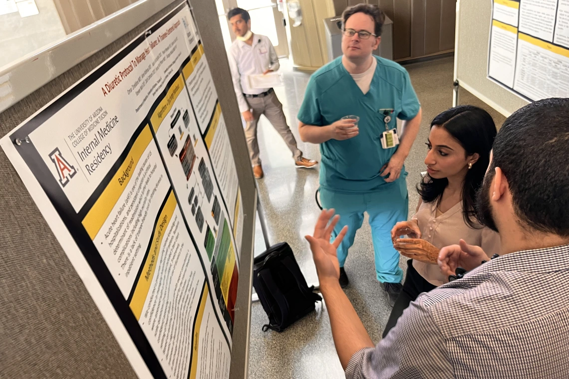 [Ryan Weyker, DO, a PGY-1 IM resident, looks at poster on diuretics while another resident discusses it with Swathi Somisetty, MD, also a PGY-1.]