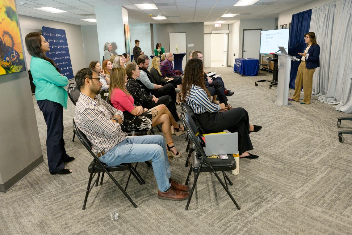 [With her division chief, Mindy Fain, MD, watching near the far pillar, and her husband Talha Riaz, MD, of the Infectious Diseases division, in the foreground, LAMS Fellowship graduate and GGP division internist Saher Khalid, MD, presents on her leadership project May 6, 2025, at the Sparking Change Celebration.]