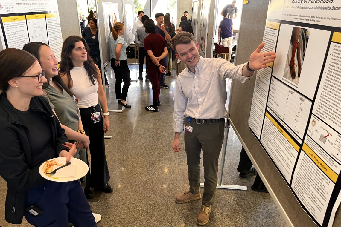 [Nathan Walton, MD, a PGY-2, talks about his poster to three IM residents, Jessica Kitsen, DO (left), Jackie Maltagliati, DO (center left), and Shenar Dinkha, DO (on right at left), all PGY-1s.]