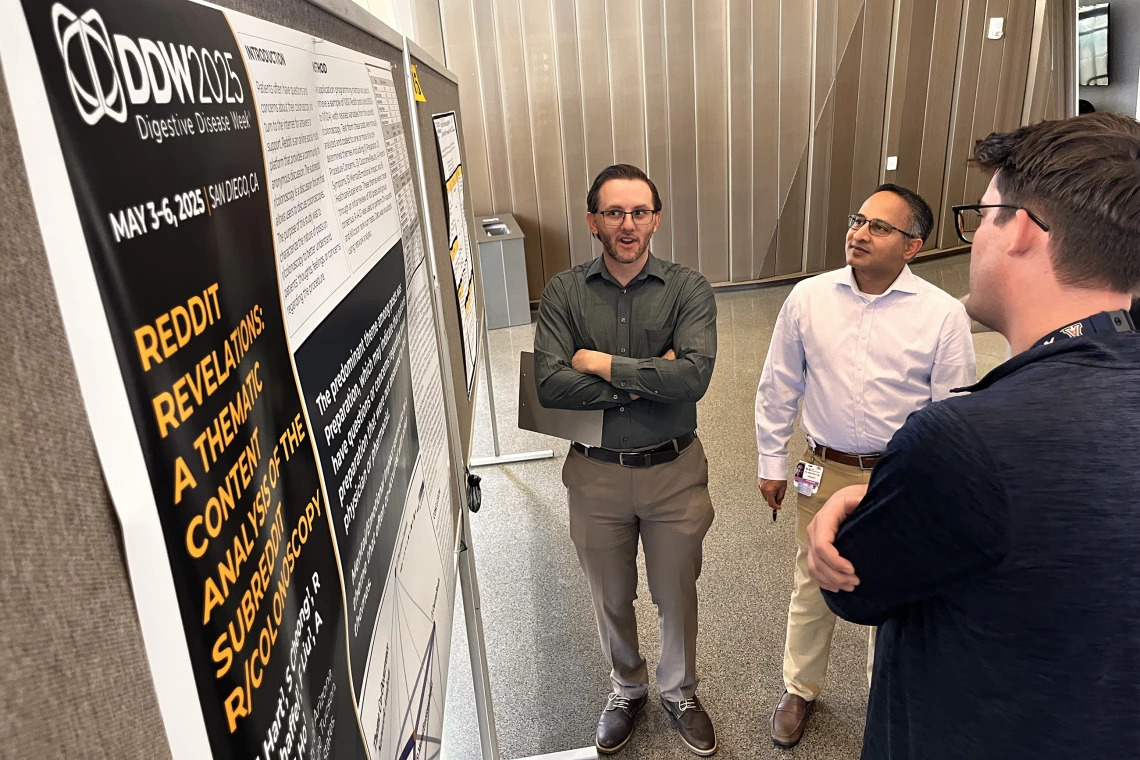 [Hospitalist Anthony Whitten, DO, asks a question about a poster, “Reddit Revelations: A Thematic Content Analysis of the Subreddit R/Colonoscopy” to Maxwell A. Hart, MD, Med, a PGY-3 IM resident, as Inpatient Medicine division chief Tejo Vemulapalli, MD, listens.]
