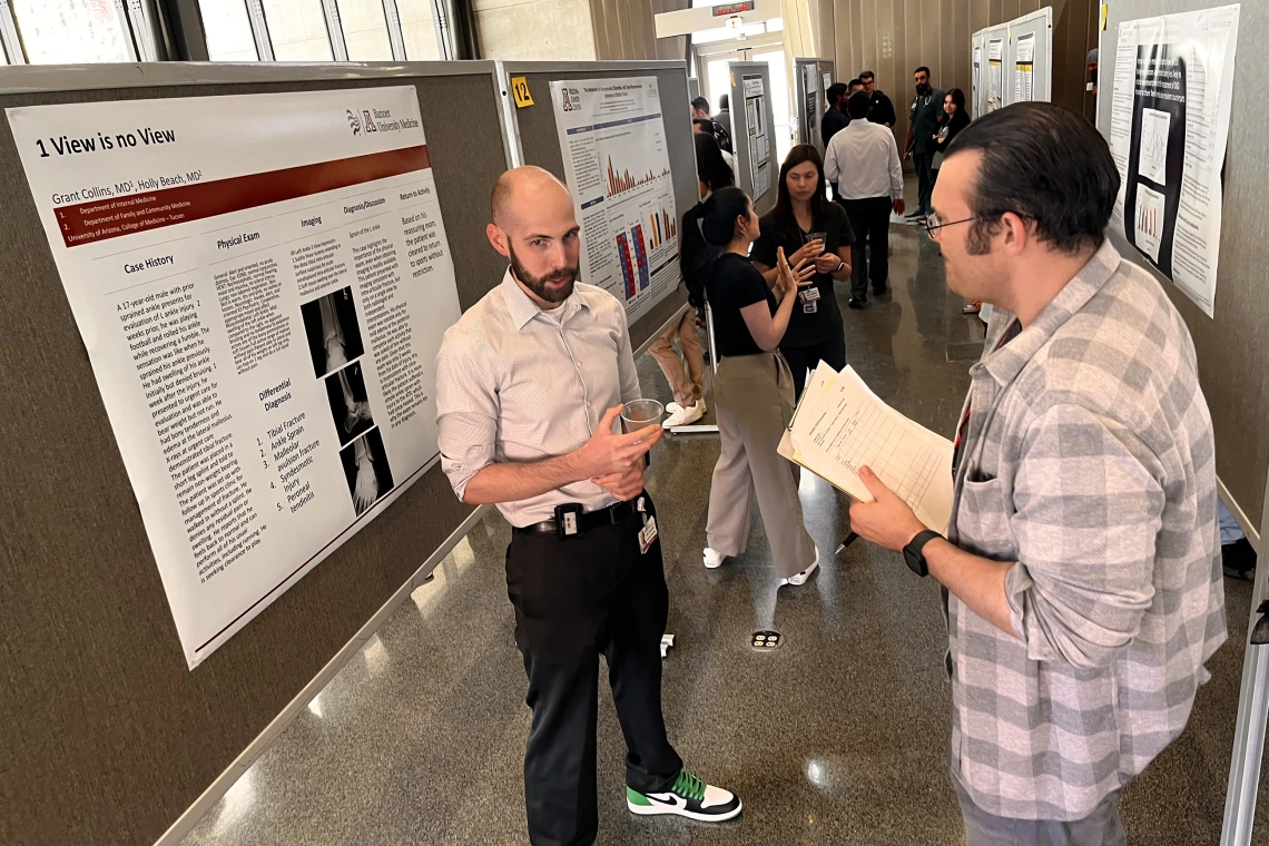 [Division of Infectious Diseases’ Alex Perry, MD, MPH, and poster author Grant Collins, MD, a PGY-2 IM resident, discuss his poster, “1 View is no View,” about a 17-year-old male injured while playing football and the need for physical exams as well as imaging in such cases.]