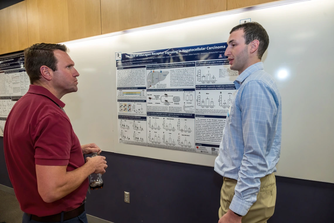 [Rheumatology’s Joshua Farr, PhD, speaks with Thadeus Carolyn, a student who works with Endocrinology’s Jennifer Stern, PhD, about a research poster on, “The role of glucagon receptor signaling in hepatocellular carcinoma.”]