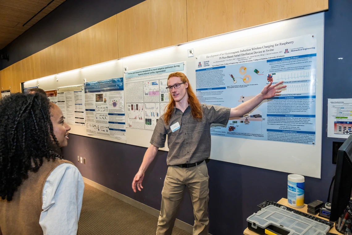 [Jesse Riemenschneider, an undergraduate student researcher with Steven Goldman, MD, talks to a SOAR in the DOM forum attendee on his poster, “Development of an electromagnetic induction wireless charging for raspberry pi pico-based atrial fibrillation device in swine.”]