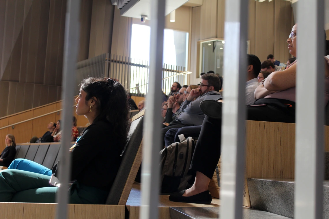 [PGY-2 IM resident Amrutha Doniparthi, MD (left) listens to the final Oral Presentation, as the judges (one row behind) consider the merits of the presenter’s research and presentation. She was among six residents who won for Best QI Project: “Improving pneumococcal vaccination rates in the resident clinic.”]