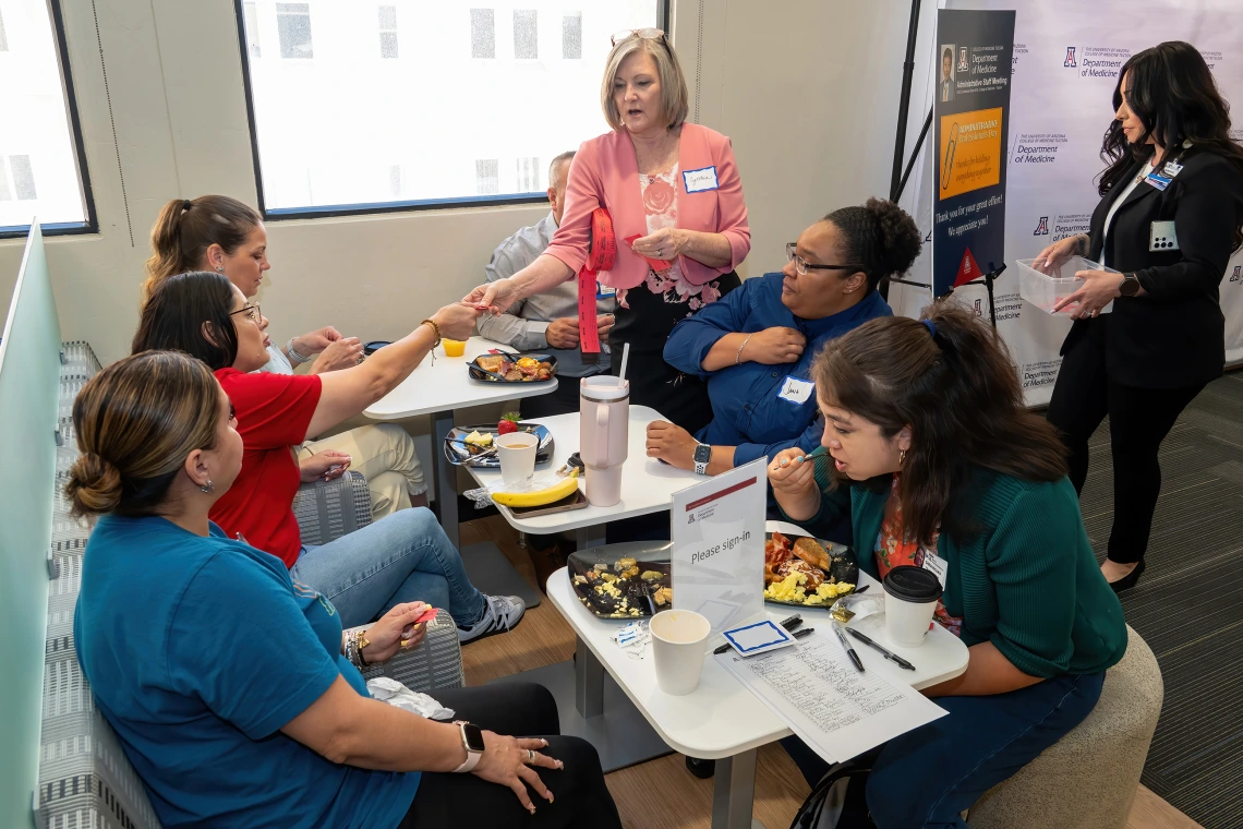 [Cynthia Campas (standing center), DOM associate administrator, and Dominica Padilla (standing right), DOM operations support manager, pass out raffle tickets for prizes to be won later to attendees of the 2025 DOM Administrative Professionals Day breakfast.]