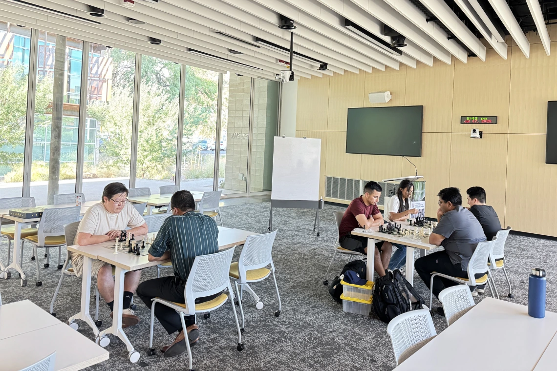 [Inaugural WellDOM Chess Club meeting participants lock in on moves they’d like to make: (table on left) Steve Sainbayar, DO (PGY-3 IM resident) and Nephrology’s Bijin Thajudeen, MD; (table on right) Asael Nuñez, MD (PGY-2 IM resident – in maroon top), Inpatient Medicine’s Anil Potharaju, MD, and Nathan Holt, DO (PGY-1 radiology resident – in black top), and his wife.]