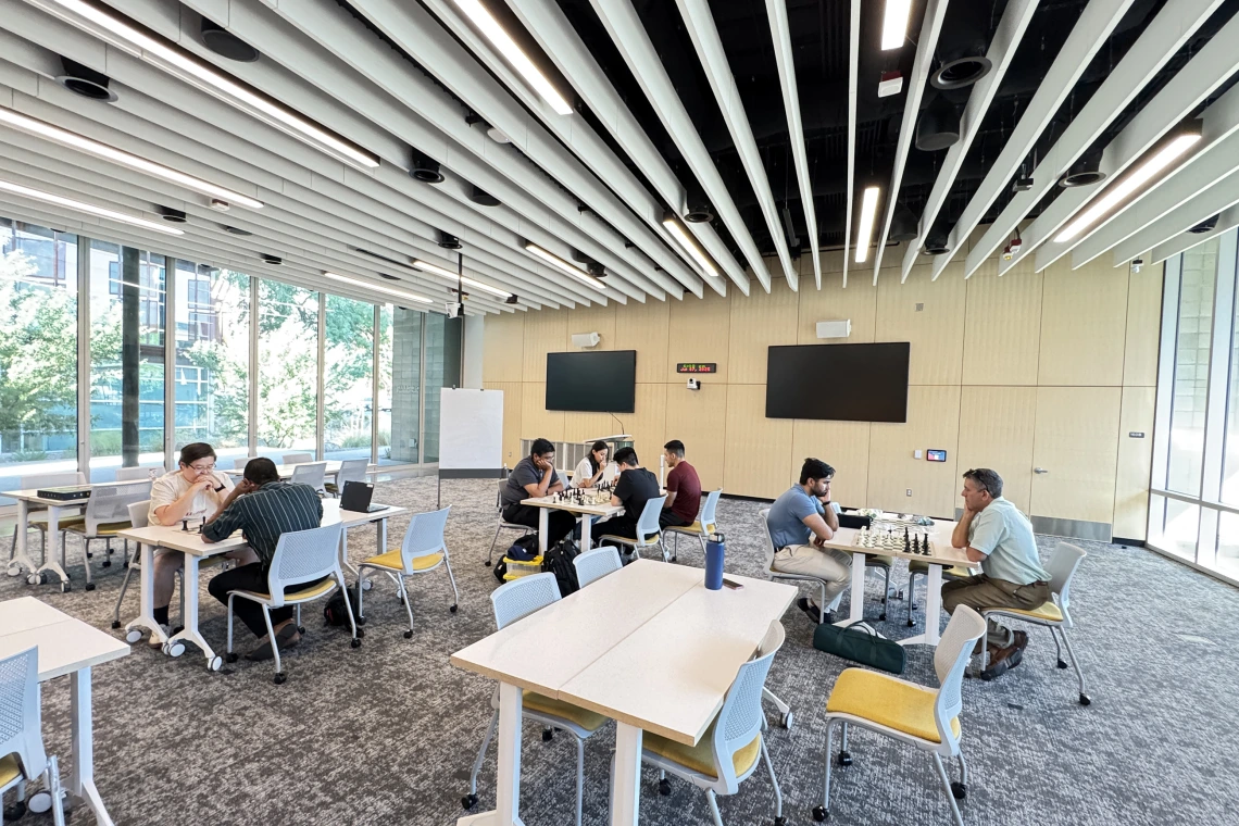 [At each table, chess players chat with each other about moves they’re making learning from more experienced players in the process and finding out more about them, their backgrounds and what sparked their interest in “the king’s game.”]