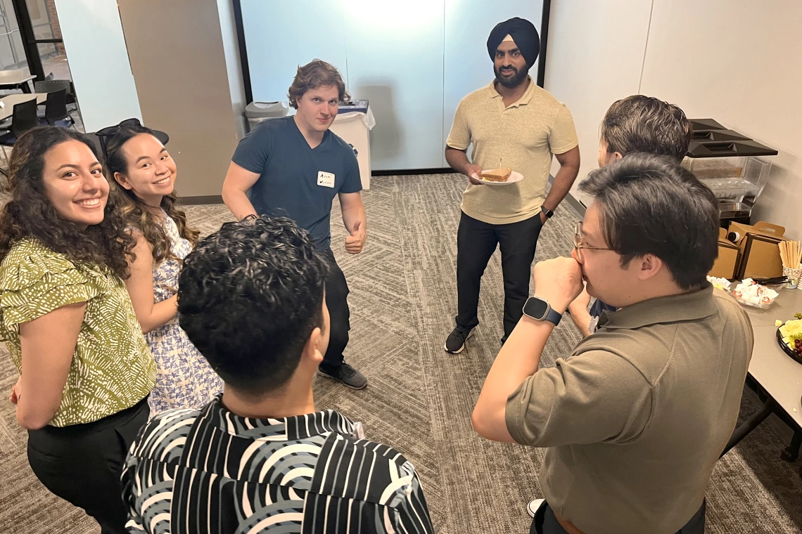 [A PGY-3 IM resident Simar Singh, MD, PhD, MS (with plate upper right), holds court at the IM Research Mixer, June 30, in the COM-T Social Hall with (to the left of him) interns Adam Weston, MD (giving thumbs up), Nellie Tolliver, MD, Joy Eskandar, MD, and others enjoying the moment.]