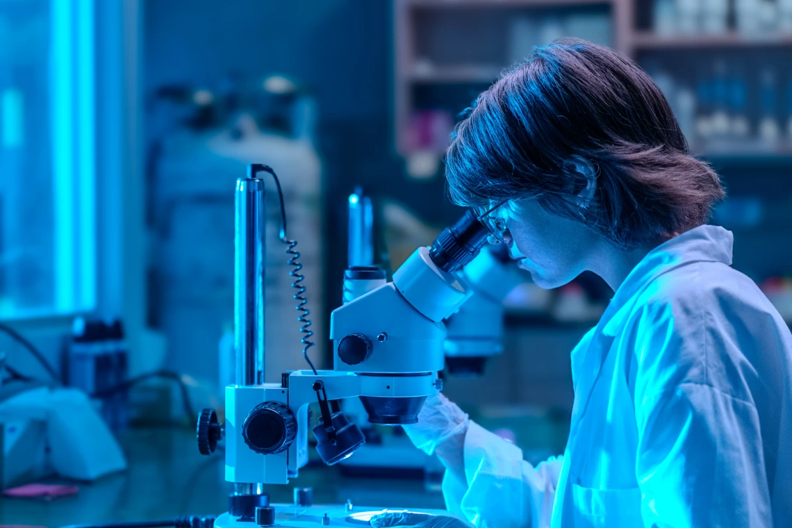 a student in a lab coat looking through a microschope