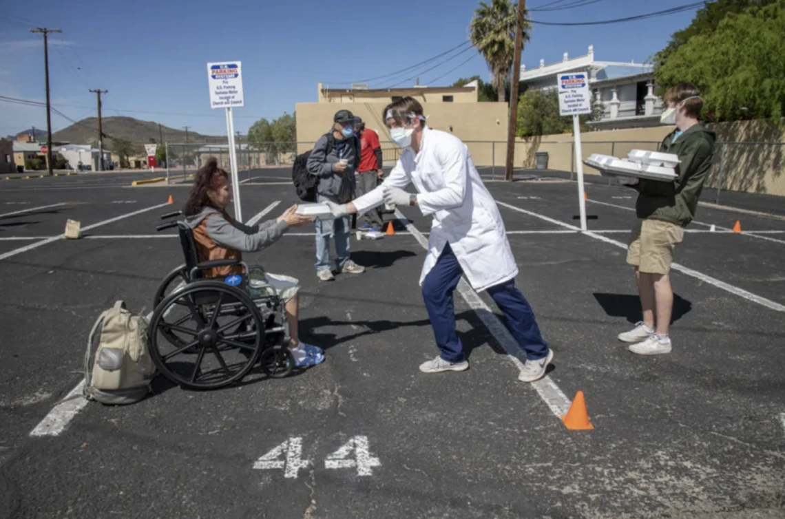A medical student hands a box of food to a community member at a volunteer site.