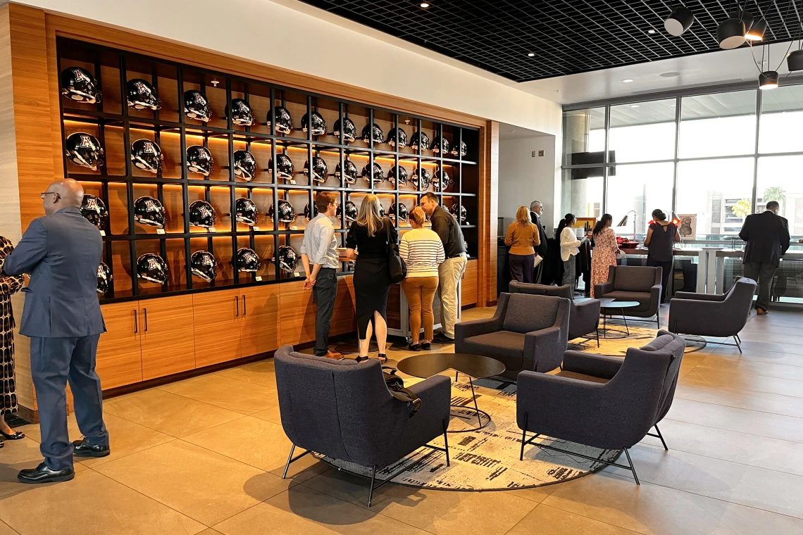 [Lining up for eats in the hall of helmets at the Arizona Sands Club, which overlooks the Arizona Wildcats football field to the south and, to the north, a training field, the main library and Catalina Mountains.]